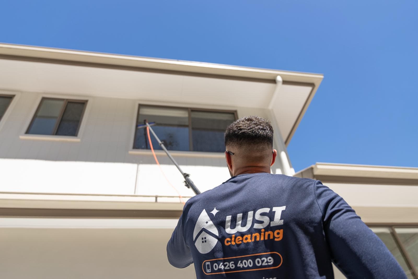 Professional window cleaner using a deionised-water pole system on a Brisbane Queenslander